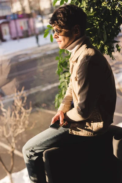 Bel homme élégant dans les lunettes de soleil tenant smartphone — Photo de stock