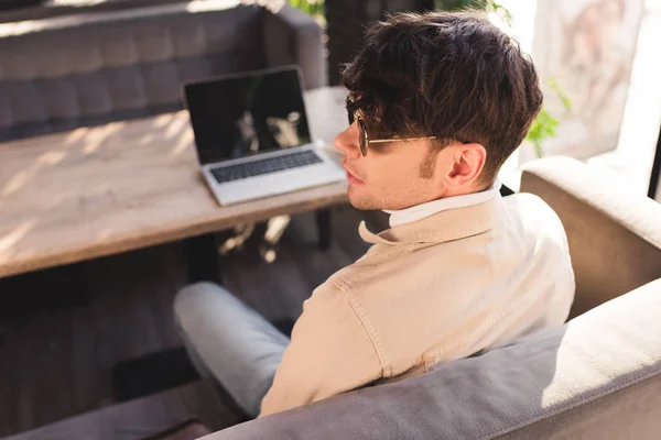 Selective focus of trendy man in sunglasses sitting near laptop in cafe — Stock Photo