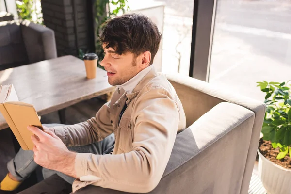 Schöner Mann lächelt, während er im Café Buch liest — Stockfoto