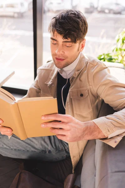 Hombre feliz sonriendo mientras lee libro en la cafetería - foto de stock