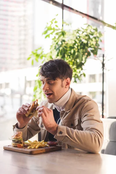 Cheerful man eating tasty burger in cafe — Stock Photo