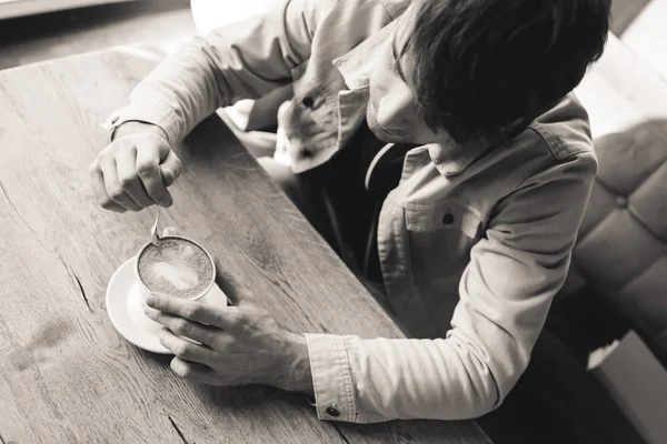 Overhead view of man holding spoon near cup with cappuccino in cafe, black and white photography — Stock Photo