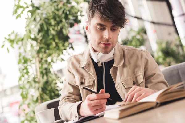 Pensive man holding pen near notebook and cup with cappuccino in cafe — Stock Photo
