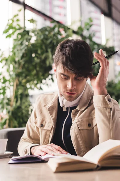 Hombre centrado leer libro y la celebración de la pluma en la cafetería - foto de stock