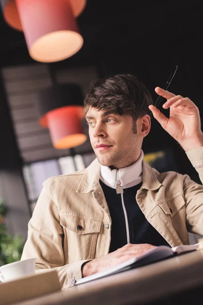 Selective focus of man sitting in in cafe and holding pen in hand in cafe — Stock Photo