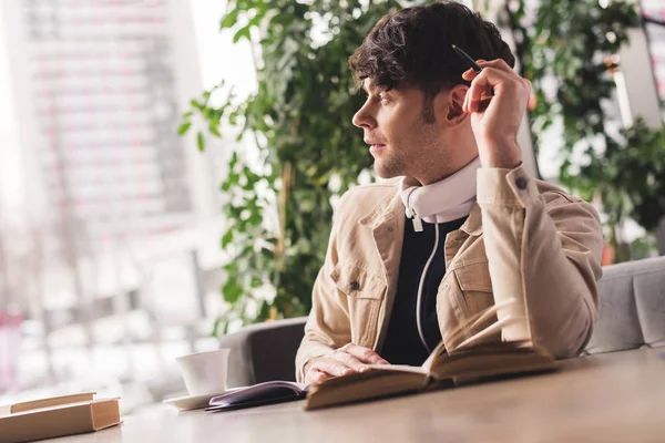 Enfoque selectivo del hombre sentado en la cafetería y la celebración de la pluma en la mano cerca de los libros - foto de stock