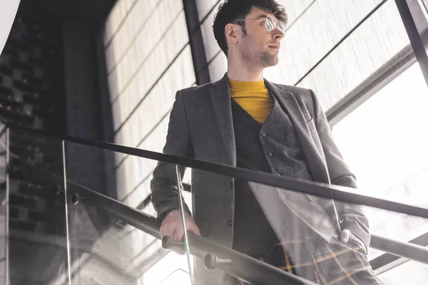 Homme élégant dans des lunettes debout avec la main dans la poche sur les escaliers — Photo de stock