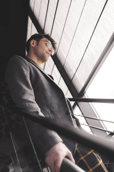 Stilvoller junger Mann mit Brille steht auf der Treppe — Stockfoto