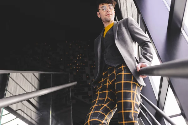 Jeune homme élégant dans des lunettes debout sur les escaliers près des fenêtres — Photo de stock