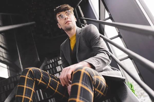 Verträumter stylischer Mann mit Brille sitzt auf der Treppe neben den Fenstern — Stockfoto