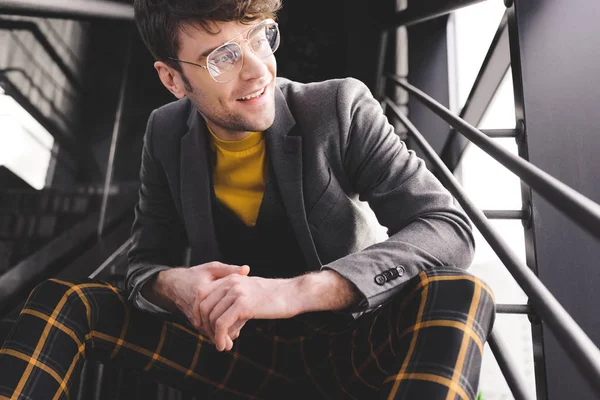 Smiling stylish man in glasses sitting on stairs near windows — Stock Photo