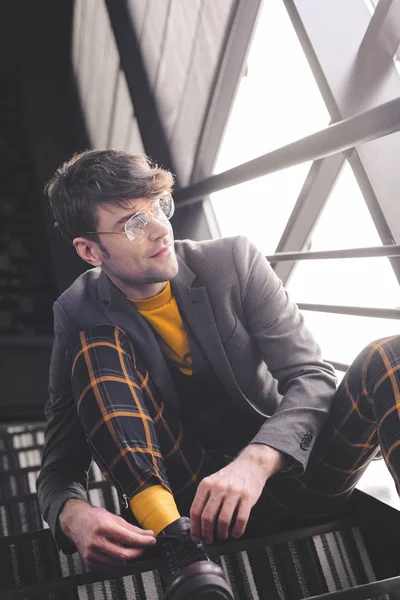 Glücklicher, stilvoller Mann mit Brille, der auf der Treppe neben den Fenstern sitzt — Stockfoto