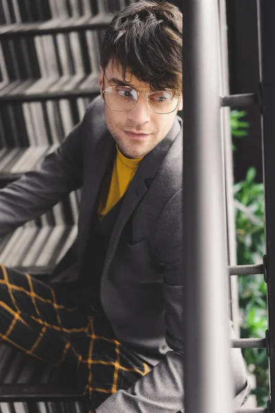 Мечтательный молодой человек в очках сидит на лестнице — стоковое фото