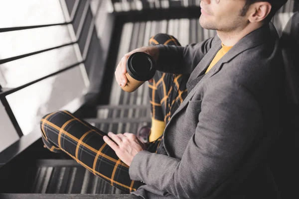 Cropped view of man sitting on stairs and holding paper cup with coffee — Stock Photo