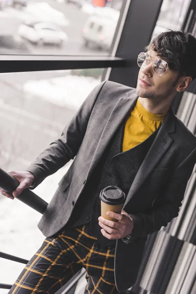 Homme dans des lunettes debout sur les escaliers et tenant tasse en papier avec café — Photo de stock