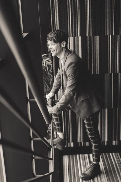 Trendiger junger Mann mit Sonnenbrille, der auf der Treppe lächelt, Schwarz-Weiß-Fotografie — Stockfoto
