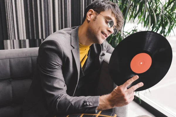 Cheerful young man in sunglasses looking at vinyl record — Stock Photo