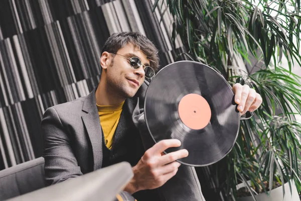 Stilvoller junger Mann mit Sonnenbrille schaut auf Schallplatte — Stockfoto