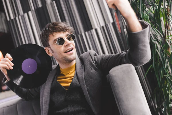 Joven feliz en gafas de sol mirando el disco de vinilo vintage - foto de stock