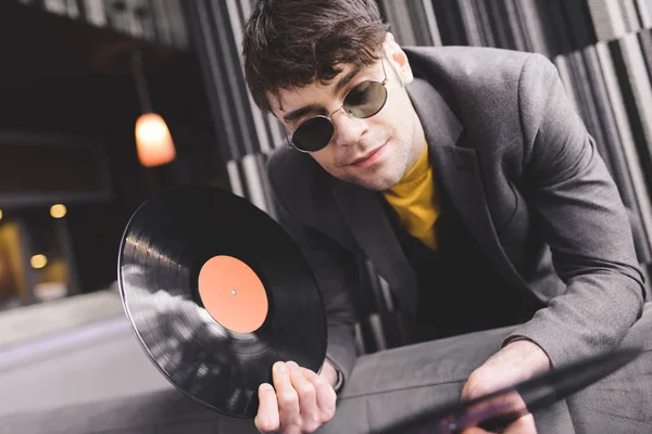 Bello giovane uomo in occhiali da sole guardando dischi in vinile retrò — Foto stock