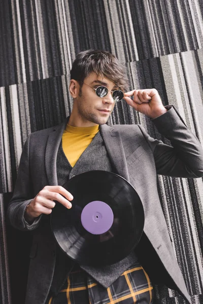 Cheerful young man touching sunglasses and holding plastic retro vinyl record — Stock Photo