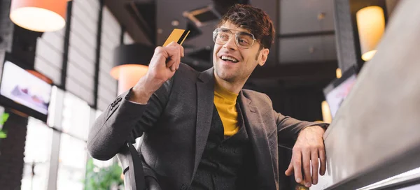 Щасливий чоловік в окулярах сидить за барною стійкою, тримаючи кредитну картку в кафе — стокове фото