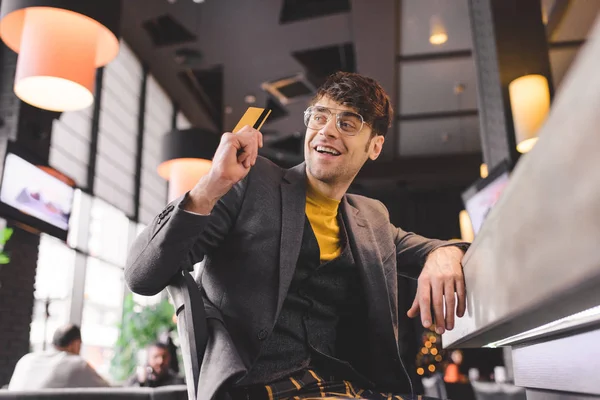 Homem sorridente em óculos sentado no balcão do bar enquanto segurava o cartão de crédito no café — Fotografia de Stock