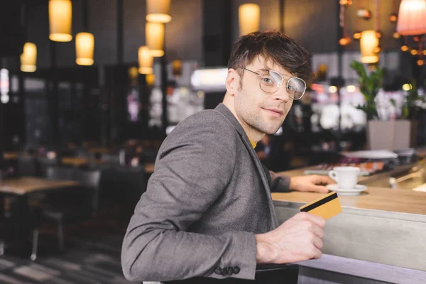 Enfoque selectivo del hombre en vasos sentados en el mostrador del bar mientras sostiene la tarjeta de crédito en la cafetería - foto de stock