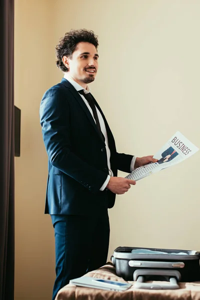 Бізнесмен тримає ділову газету біля ліжка з багажем в готельному номері — стокове фото