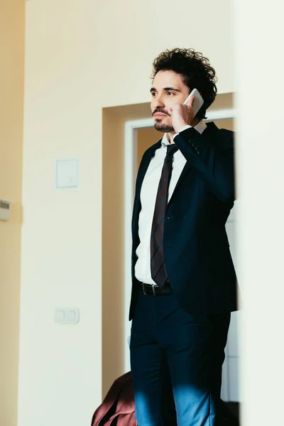 Homem de negócios de terno falando no smartphone durante viagem de negócios no quarto de hotel — Fotografia de Stock