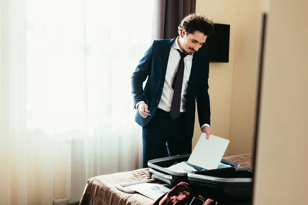 Hombre de negocios adulto poner portátil en la maleta en la cama en la habitación de hotel — Stock Photo