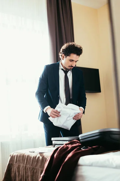 Adult businessman putting clothes in suitcase on bed in hotel room — Stock Photo