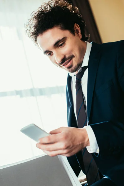 Hombre de negocios guapo hablando en el teléfono inteligente y la celebración de documentos en la habitación de hotel - foto de stock