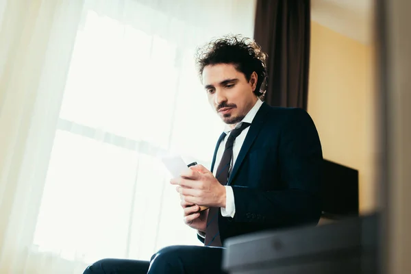 Handsome adult businessman using smartphone in hotel room — Stock Photo