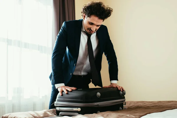 Красивий бізнесмен у костюмі з валізою на ліжку в готельному номері — стокове фото