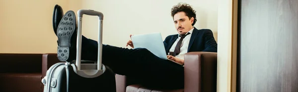 Hombre de negocios en red en el portátil con las piernas en la maleta en la habitación del hotel - foto de stock