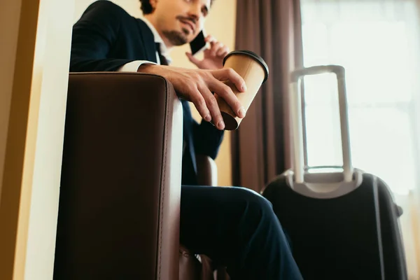 Geschäftsmann mit Einwegkaffee redet mit Smartphone im Hotelzimmer mit Koffer — Stockfoto