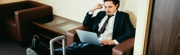 Adult businessman working on laptop with legs on suitcase in hotel room — Stock Photo