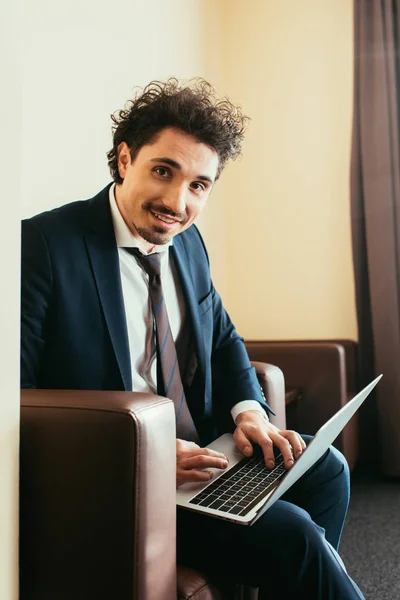 Uomo d'affari sorridente in tuta che lavora su laptop in camera d'albergo — Foto stock
