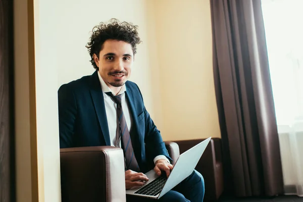 Cheerful businessman in suit working on laptop in hotel room — Stock Photo