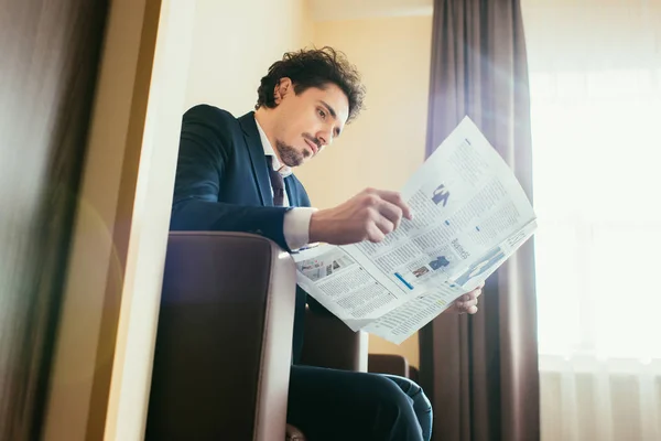 Homme d'affaires en tenue formelle lecture journal dans la chambre d'hôtel avec lumière du soleil — Stock Photo