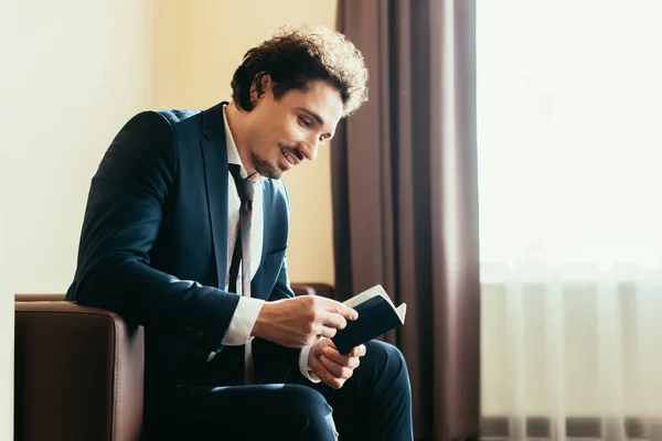 Улыбающийся бизнесмен с паспортом и сидящий в номере отеля — стоковое фото
