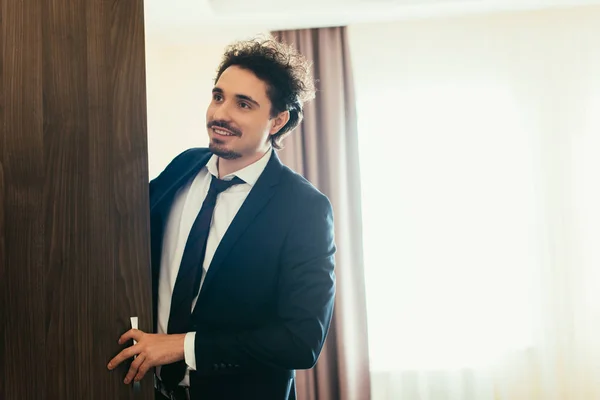 Schöner lächelnder Geschäftsmann öffnet Kleiderschrank im Hotelzimmer — Stockfoto