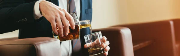 Vista recortada del hombre de negocios vertiendo whisky de botella en vidrio en la habitación de hotel - foto de stock