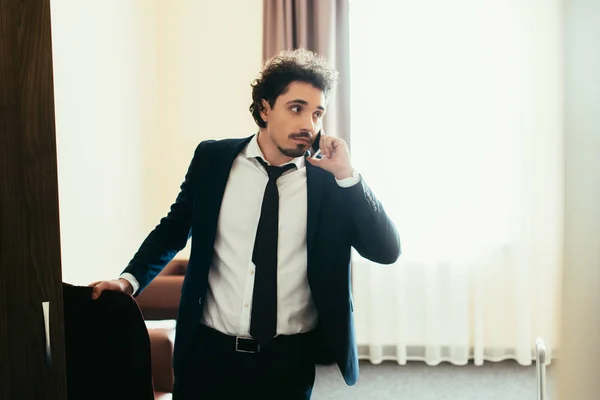 Handsome businessman talking on smartphone during business trip in hotel room — Stock Photo