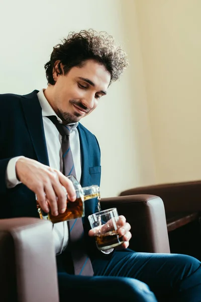 Sonriente hombre de negocios vertiendo whisky en el vaso en la habitación del hotel - foto de stock