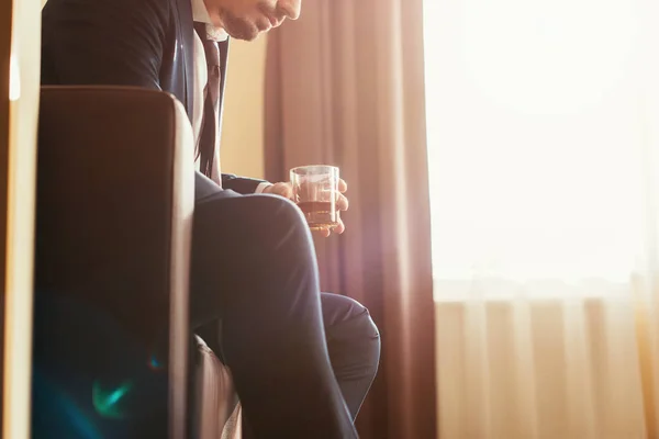 Vista ritagliata di uomo d'affari sconvolto in abbigliamento formale in possesso di un bicchiere di whisky in camera d'albergo — Foto stock
