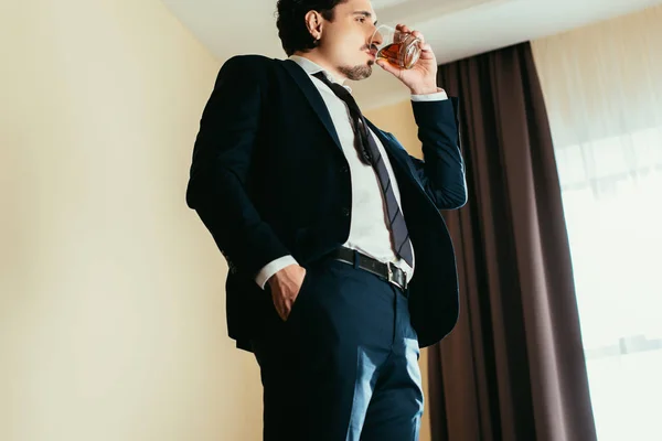 Hombre de negocios bebiendo whisky de cristal en la habitación de hotel - foto de stock