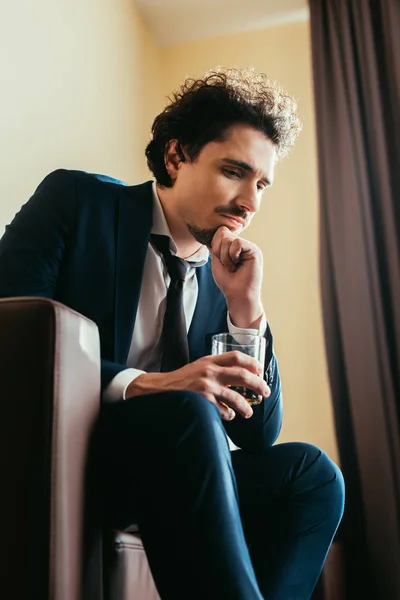 Upset businessman in formal wear holding glass of whiskey in hotel room — Stock Photo