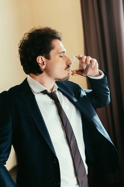 Бизнесмен в костюме пьет виски из стекла в номере отеля — стоковое фото